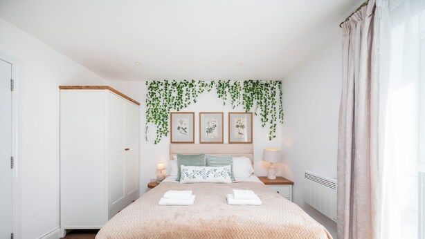 A bedroom with a bed, nightstands, a window with curtains, a radiator, and wall-mounted greenery. - Modern Luxury 4Bdrm 15 min to LDN centre | Business/Vacay | Parking onsite (London)
