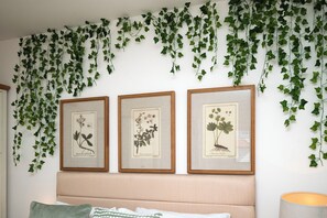 Ein Schlafzimmer mit einem Kopfteil, einem Bett mit Kissen und drei gerahmten Pflanzenabbildungen an der Wand.
