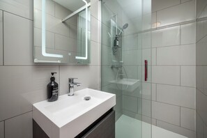 Ein modernes Badezimmer mit einem weißen Waschbecken, einer Duschkabine aus Glas und einem Spiegel mit LED-Beleuchtung.