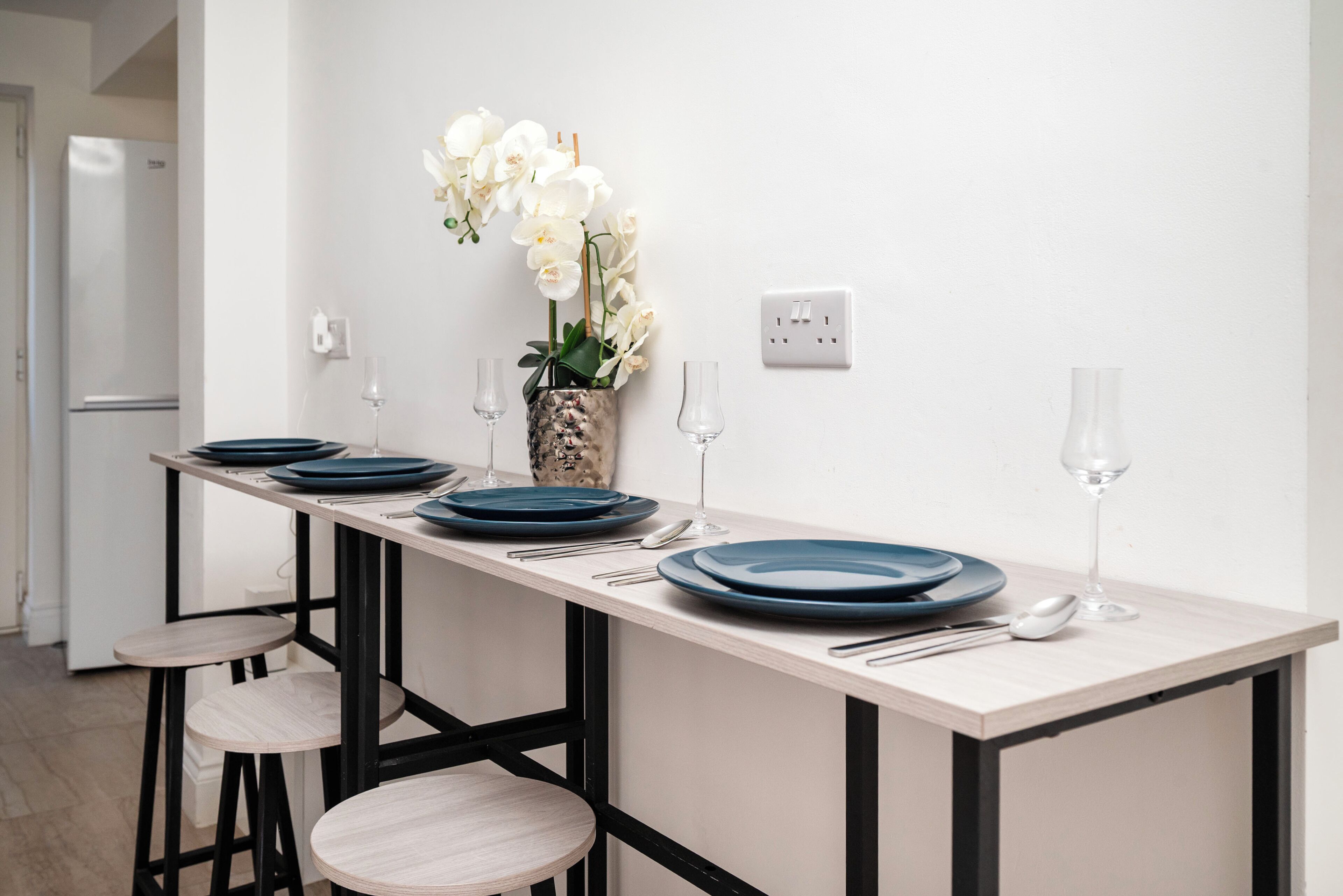 Une cuisine avec un grand îlot central, des tabourets et des orchidées blanches.