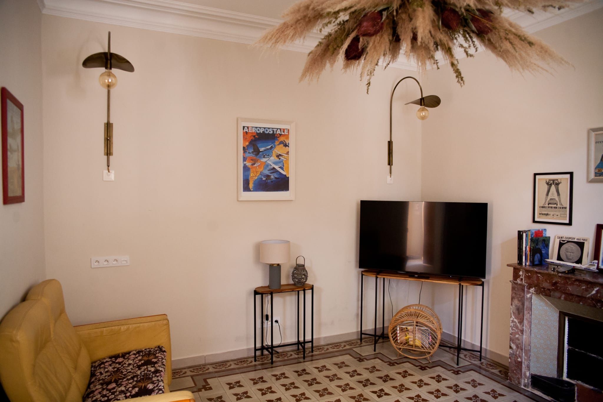 Een woonkamer met een bank, een televisie, een lamp, een poster en een open haard.