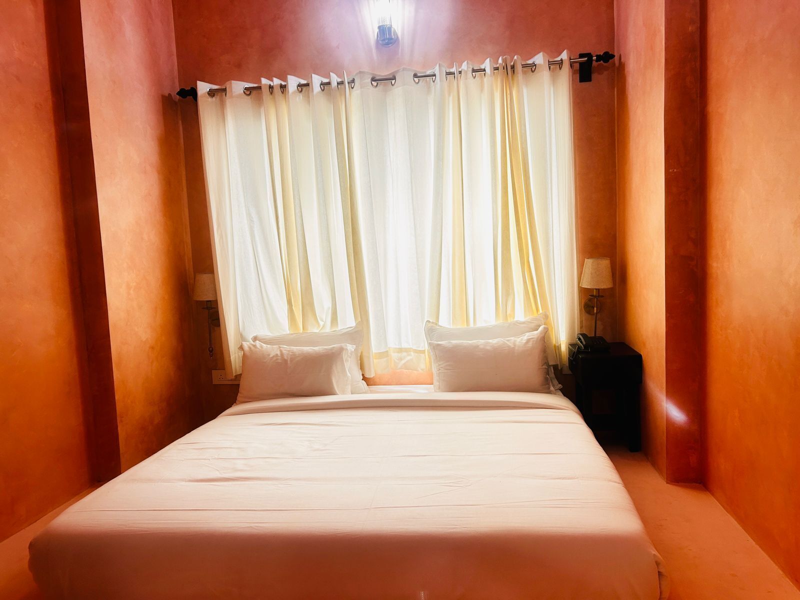 A hotel room with a large bed, white bedding, and a view through sheer curtains.