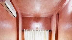 A narrow, single-room hotel room with a bed, curtains, bedside lamps, and a wall-mounted air conditioner. - SADRI HAVELI Boutique Heritage Hotel - Lake Pichola Udaipur (Udaipur)