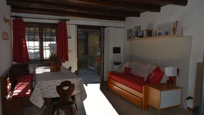 A cozy room with a wooden bench, a table with a floral tablecloth, a sofa with red cushions, and a small bedside table with a lamp. - Gio's house, apartment with garden and barbecue, relaxation in the midst of nature (ville sur sarre)