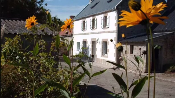 Un bâtiment blanc avec un toit gris, entouré de verdure et de fleurs.