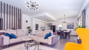 Ein modernes Wohnzimmer mit einem Ecksofa, einem leuchtend gelben Sessel und einem Essbereich im Hintergrund.