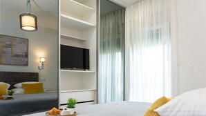 Ein modernes Hotelzimmer mit einem Bett, einem Flachbildfernseher, einem großen Spiegel und einem Frühstückswagen.