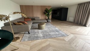 A modern living room with a sofa, a floor lamp, a potted plant, and a herringbone-patterned floor. - Eco Forest Home by Palette Resort De-steppe (Ulicoten)