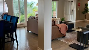 A modern living room with a dining area, large windows, and a view of greenery outside. - Sunset Summit by Coastline Vacation Rentals (La Mesa)