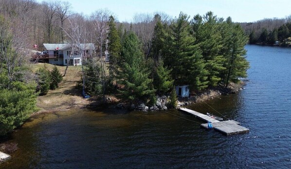 A lakeside cabin with a dock extending into the water, surrounded by dense forest.