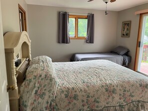 A bedroom with a large bed, a smaller bed, a dresser, a window with curtains, and a ceiling fan.
