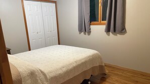 Un dormitorio con cama, una puerta, una ventana con cortinas y suelo de madera.