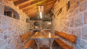 Una stanza con pareti in pietra, un tavolo e panche in legno, un camino e una lampada a sospensione.
