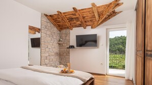 Camera da letto con parete in pietra, travi in legno a soffitto, un letto, una TV e un balcone con vista.
