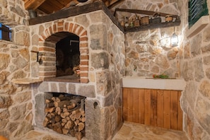A stone fireplace with a brick arch, a wood-burning stove, and a stack of firewood. - Cozy Villa for 8 With Pool and Jacuzzi (Proložac)