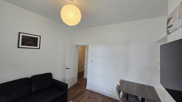 A room with a black sofa, a dining table with chairs, a hanging light fixture, and a door leading to another room. - Free Parking + Modern 1BR Near Central London (Greater London)