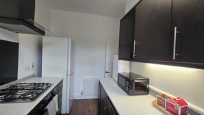 A modern kitchen with a gas stove, white refrigerator, black cabinets, and a toaster. - Free Parking + Modern 1BR Near Central London (Greater London)