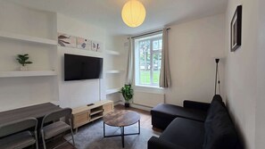 A living room with a TV, sofa, and a window with curtains. - Free Parking + Modern 1BR Near Central London (Greater London)