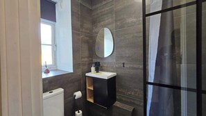 A bathroom with a toilet, a sink with a mirror, a shower area, and a window with a curtain. - Free Parking + Modern 1BR Near Central London (Greater London)