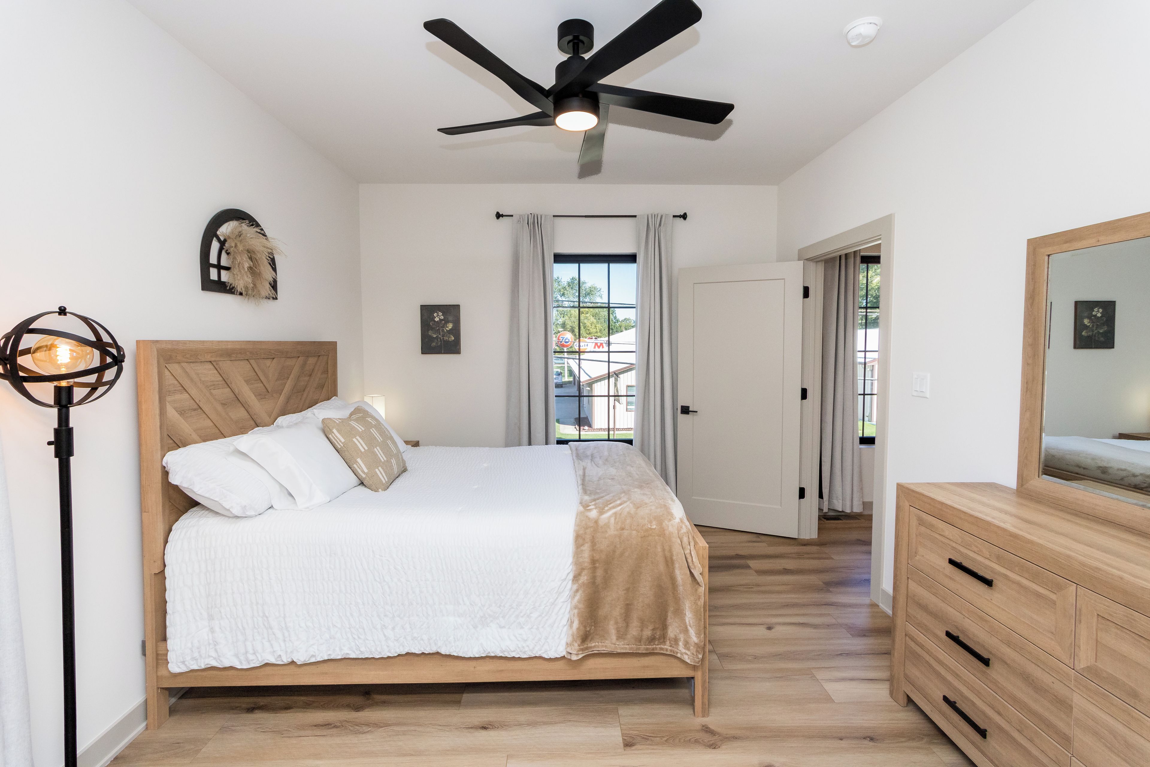 A bedroom with a bed, a ceiling fan, a dresser, and a window with curtains.