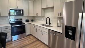 A modern kitchen with white cabinets, stainless steel appliances, and a wooden floor.