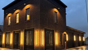 A two-story brick building with large windows and doors, illuminated by vertical light strips.