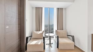 Een moderne hotelkamer met een groot raam, twee banken, een klein rond tafeltje en een houten garderobe.
