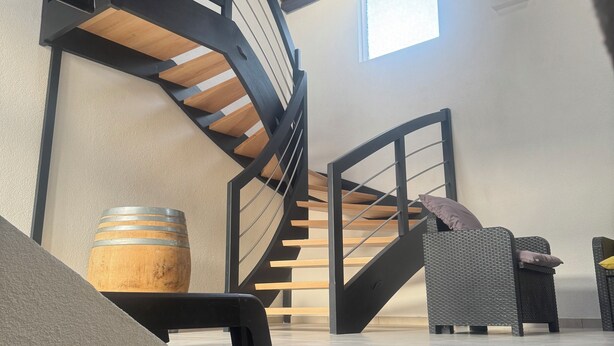 A modern interior with a spiral staircase, a wooden barrel, and wicker furniture.