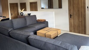 A modern living room with a grey sectional sofa, a wooden coffee table, and a large mirror on the wall. - L'Echappée Alsacienne Vacation Rental (Geispolsheim)