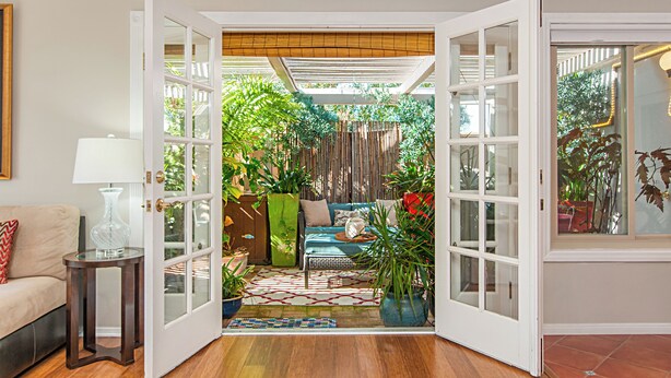 An open doorway leading to a sunlit room with a sofa, a small table, and various potted plants. - Fully Furnished 2BR Extended Stay Near UCSD & Scripps. Private Patio & Spa Bath (San Diego)