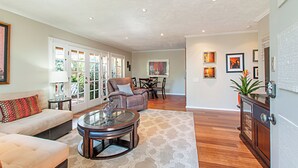 A spacious living room with a sofa, armchair, and coffee table, a dining area with chairs and a table, and a kitchen area with cabinets and a refrigerator. - Fully Furnished 2BR Extended Stay Near UCSD & Scripps. Private Patio & Spa Bath (San Diego)