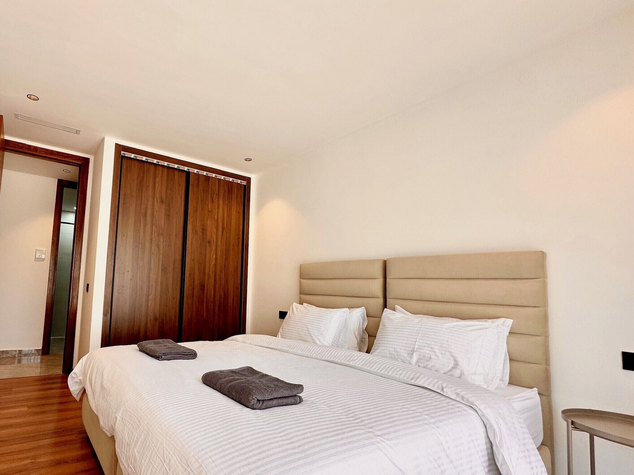 A hotel room with a large bed, a wooden wardrobe, and a small table.