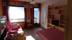 A cozy room with a wooden interior, a sofa with floral cushions, a small table, and a TV on a wooden shelf. - Refuge 66 is ideally located facing south, close to the ski slopes and hiking trails. (Saint-Aventin)
