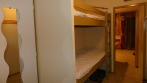 A room with bunk beds, a door with a mirror, and a small hallway leading to another room. - Refuge 66 is ideally located facing south, close to the ski slopes and hiking trails. (Saint-Aventin)
