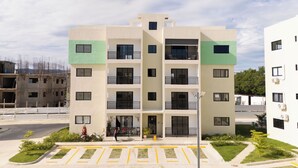Edifício residencial com várias andares, varandas, entrada com portão e área de estacionamento com vagas demarcadas.
