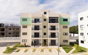 A multi-story residential building with balconies, a gated entrance, and a parking area with marked spaces. - The Jade Lodge! Beautifully decorated 2BR apartment in Puerto Plata (Canaveral del Mar)