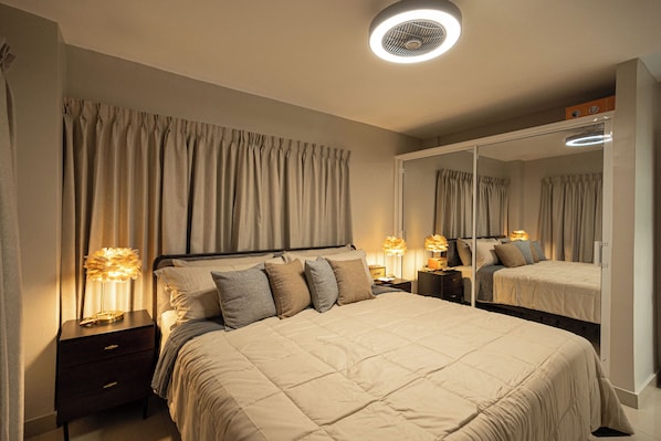 A bedroom with a large bed, two bedside tables with lamps, a mirror, and a ceiling light.
