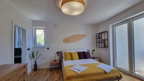 A modern bedroom with a bed, bedside tables, a wooden dresser, a large window, and a ceiling light. - Summer Color (Novalja)