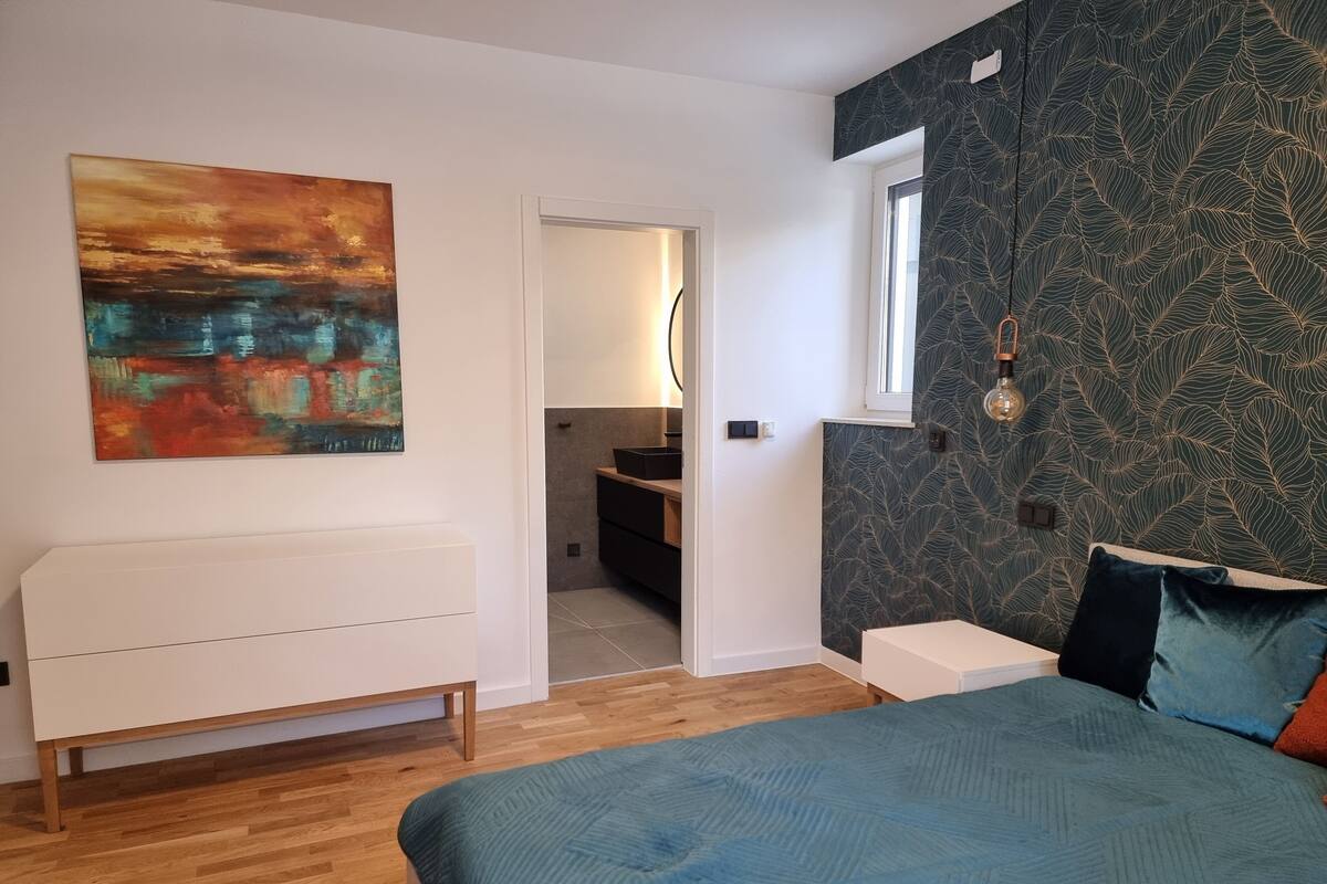 Un dormitorio con cama, cómoda, cuadro, ventana y pared con diseño.
