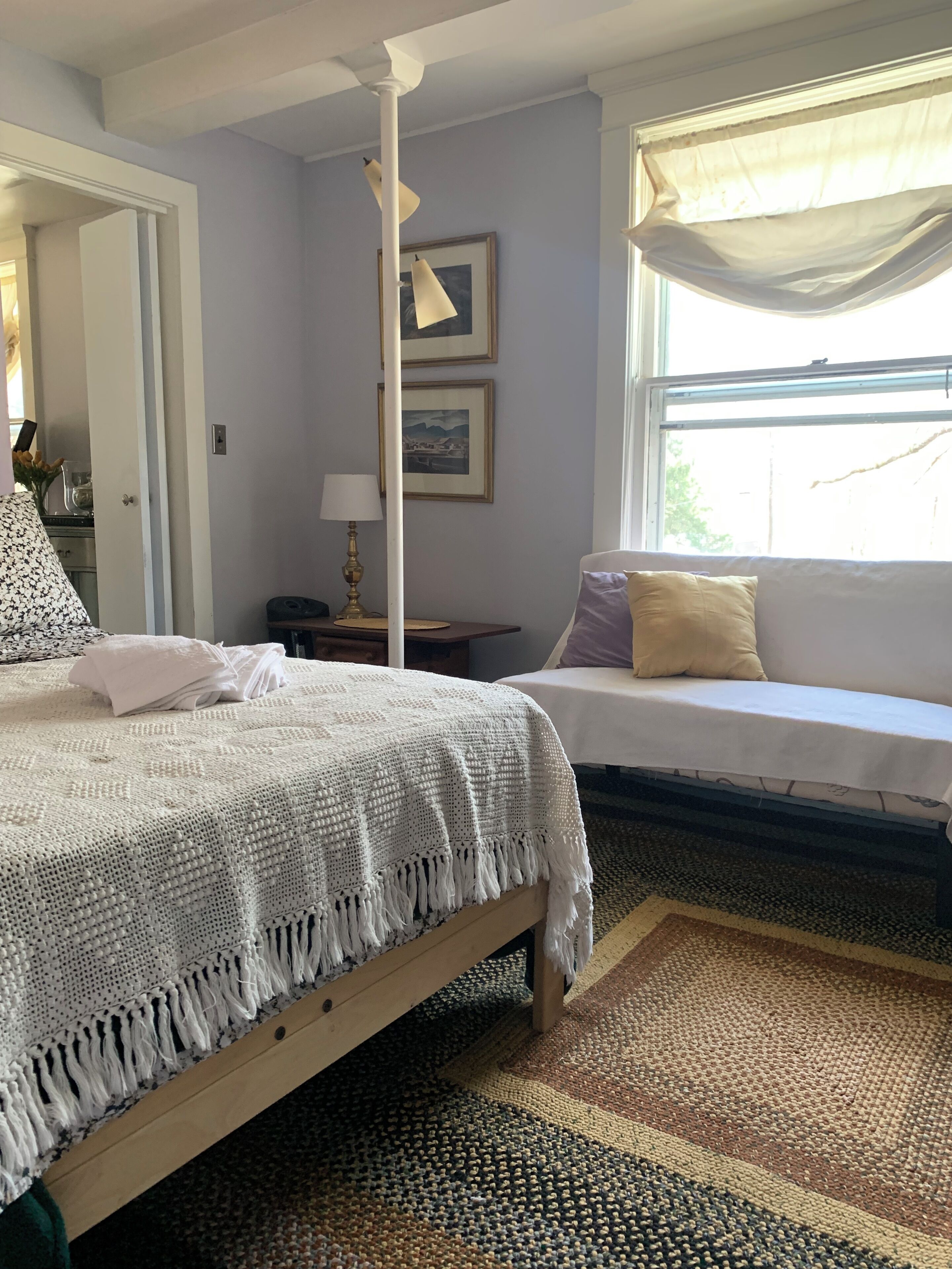 Un dormitorio con cama, mesita de noche, lámpara, ventana con cortinas y un marco de pared.