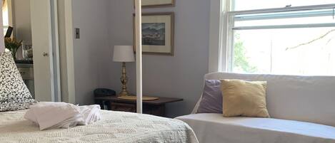 Un dormitorio con cama, mesita de noche, lámpara, ventana con cortinas y un marco de pared.