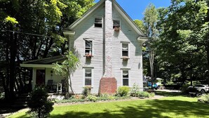 Une maison à deux étages avec une cheminée centrale, entourée d’une pelouse bien entretenue et d’arbres.