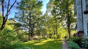 Un jardin bien entretenu, avec un chemin de pierres menant à une maison dont les fondations sont en briques et le revêtement extérieur est blanc.