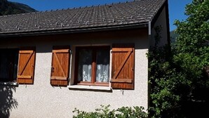 Une maison à deux étages, avec un toit en tuiles, des volets en bois et un petit porche.