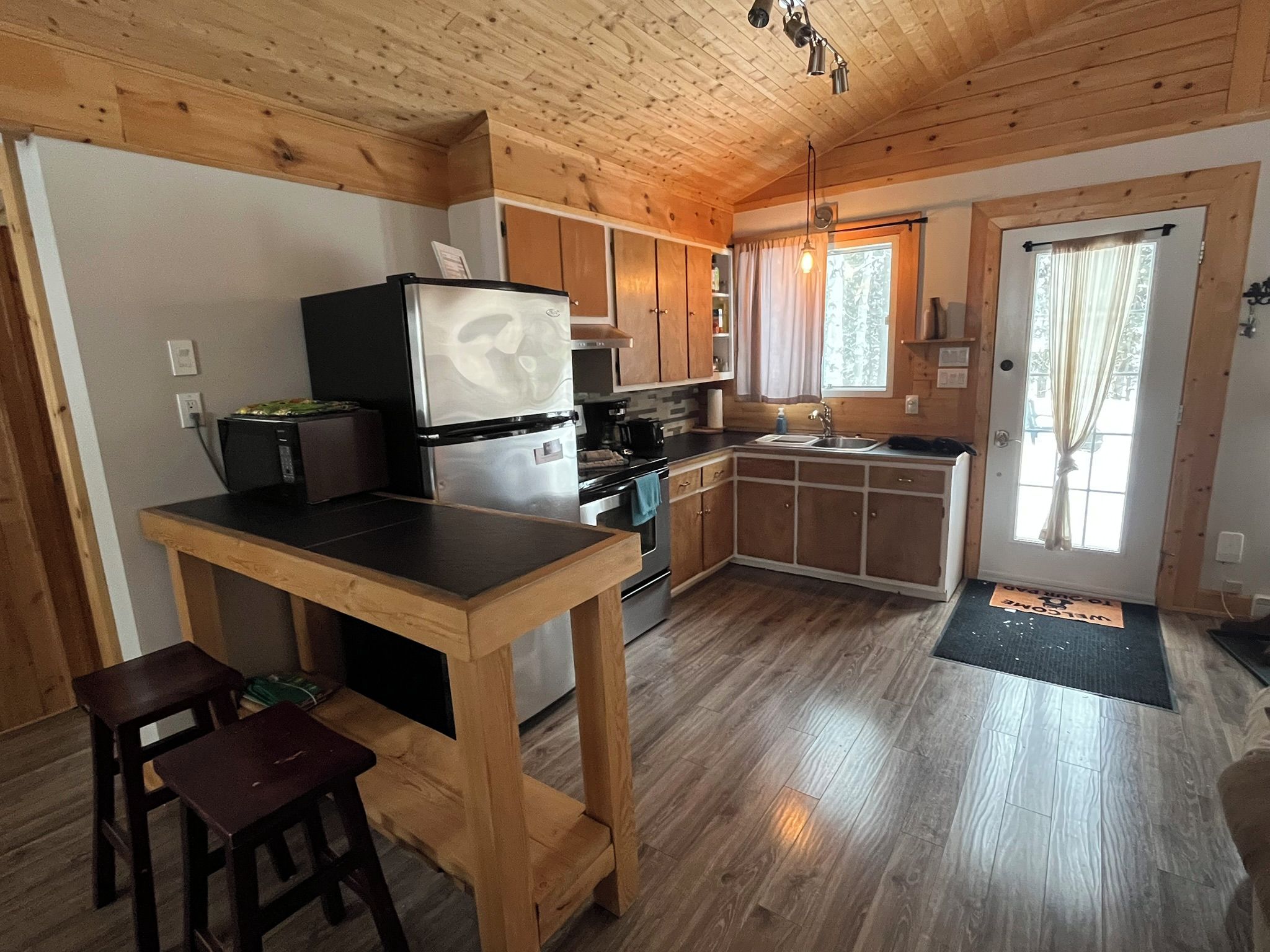 A compact kitchen with wooden cabinets, a central island, and a dining area with stools.