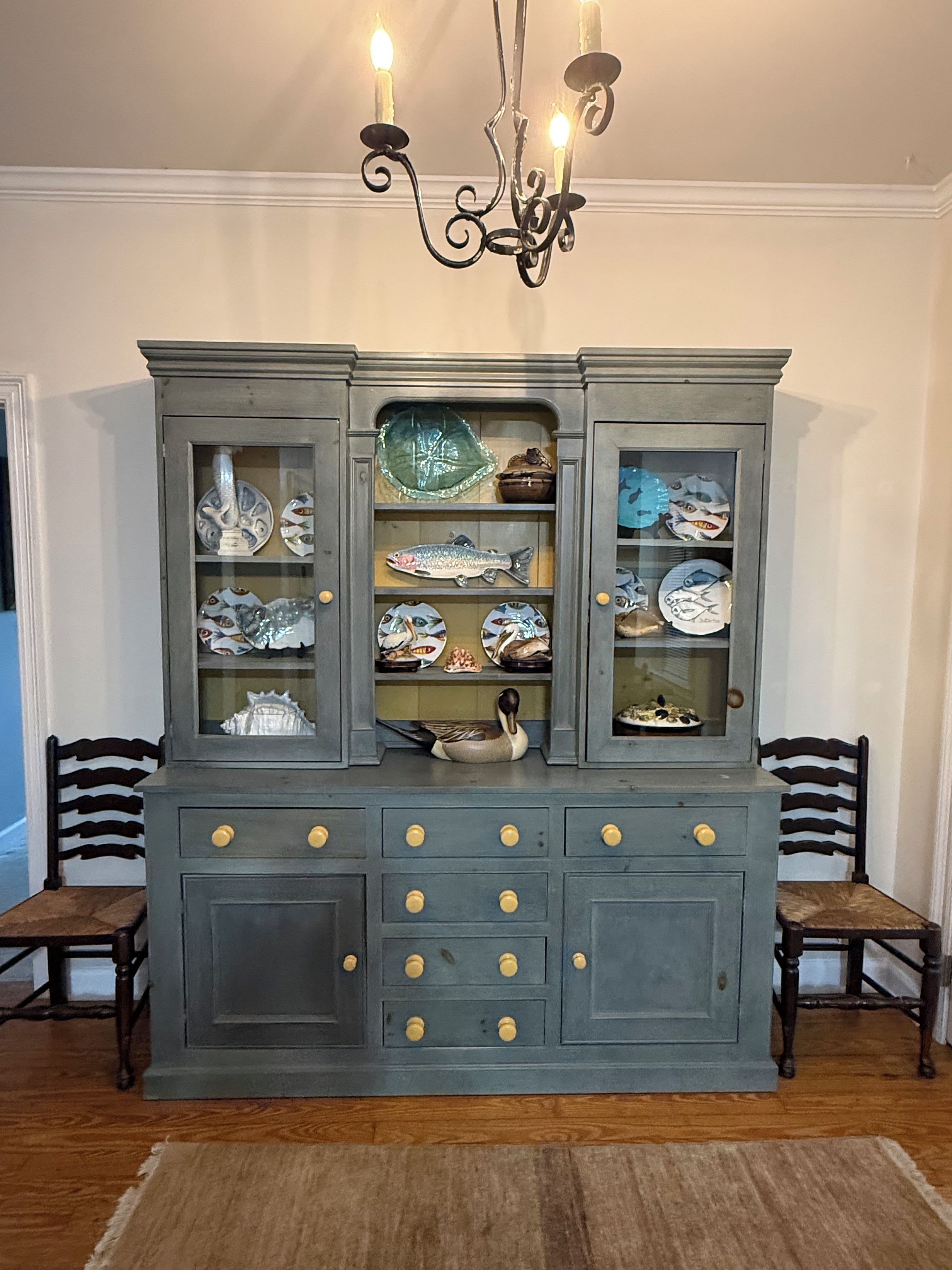 Un mueble azul oscuro con puertas de cristal que exhibe diversos platos y una figurita de pato.