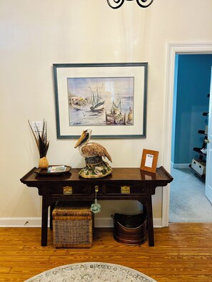 A wooden console table with a framed seascape painting, a decorative bird sculpture, a small wicker basket, and a framed picture labeled "Wifi".