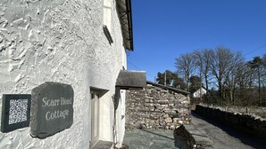 Uma casa de pedra com uma placa que diz 'Scarr Head Cottage' e um código QR.