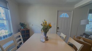 Une salle à manger avec une table, des chaises, un vase de fleurs, un radiateur et une fenêtre avec des stores.