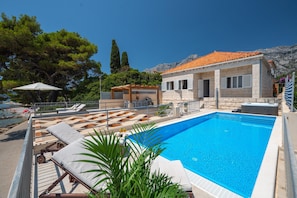 Zona de piscina con sillones de descanso, un jacuzzi y vistas al mar.